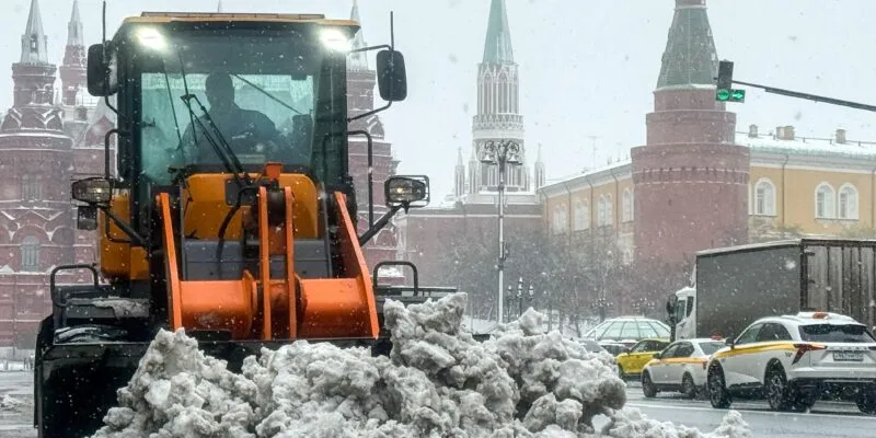Трактор сгребает кучу снега у стен московского Кремля