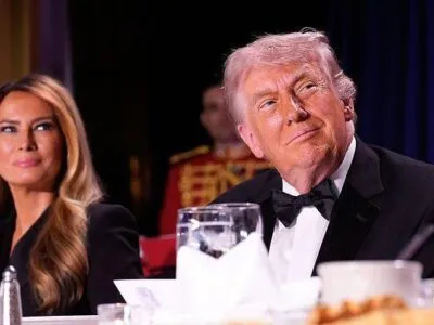 Donald Trump looks to right of frame while slightly smiling along with Melania in the background as they sit at their table during the correspondent's dinner.