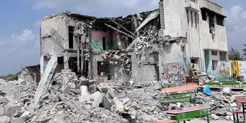 Развалины здания, возле которого стоят школьные парты.