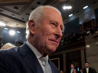 Король Карл в синем костюме в тонкую полоску, белой рубашке и светло-голубом галстуке.