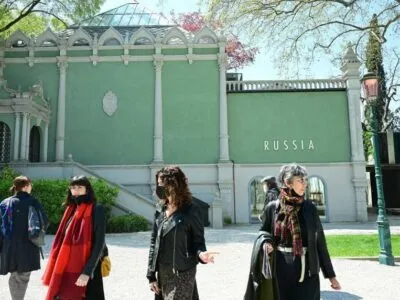 Четыре женщины, две из них в медицинских масках, идут по территории биеннале у павильона с надписью Russia.