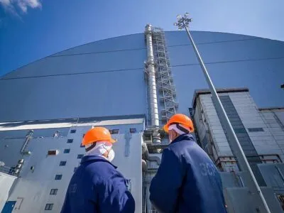 Двое работников ЧАЭС в оранжевых шлемах стоят у купола, защищающего саркофаг