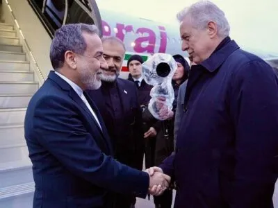 Двое мужчин пожимают друг другу руки у трапа самолета, на борту которого изображен флаг Ирана.