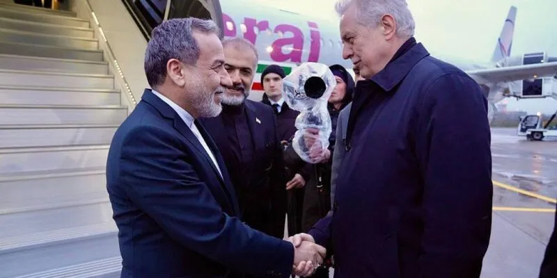 Двое мужчин пожимают друг другу руки у трапа самолета, на борту которого изображен флаг Ирана.