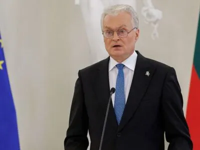Президент Литвы Гитанас Науседа за трибуной на фоне флагов Литвы и Евросоюза. Он носит очки и гладко выбрит, волосы седые. На нем черный пиджак и белая рубашка с синим галстуком.