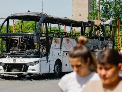 В самопровозглашенной ДНР заявили о восьми погибших при ударе по рейсовому автобусу. Что известно 2 Две женщины идут по улице, за ними — сгоревший автобус.