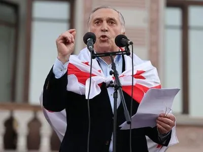 Паата Бурчуладзе, седой мужчина в черном пиджаке с накинутым на плечи грузинским флагом, говорит в два микрофона. В его левой руке бумаги