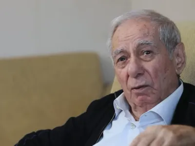 Акрам Айлисли в белой рубашке и черном жакете смотрит мимо камеры