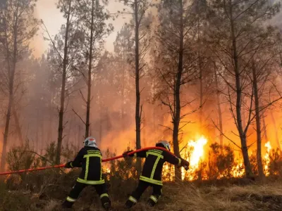 Двое пожарных тянут шланг на фоне горящего леса в районе Бордо