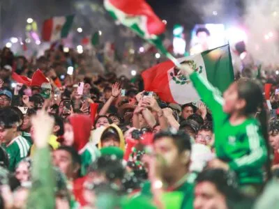 A huge crowd of fans wearing Mexico's green football kit and waving the country's flag celebrate the team's 2-0 World Cup win against Ecuador in Mexico City at night.