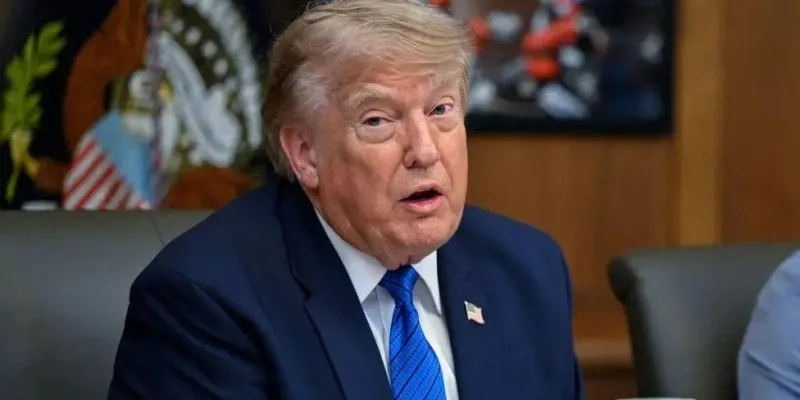Дональд Трамп на заседании кабинета министров США в Кэмп-Дэвиде 31 июля: он одет в темно-синий костюм, галстук светло-голубого цвета с черными горизонтальными полосками, белую рубашку, а на пиджаке у него прикреплен значок с изображением флага США