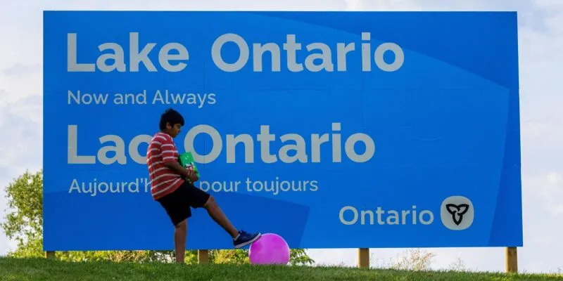 A sign reads "Lake Ontario now and always" with a boy playing with a ball nearby.