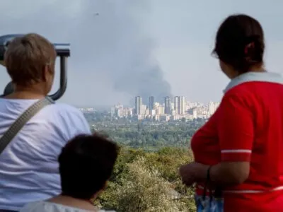 120 часов террора. Как и зачем Россия запускает волны реактивных дронов по Киеву и что Украина готовится с этим делать 2 Три женщины смотрят с возвышенности на большой столб дыма вдали, за районом многоэтажных зданий