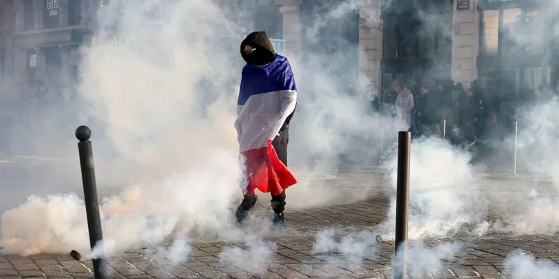 A protester wrapped in a French flag stands with smoke all around on a street in Lille on 17 October.