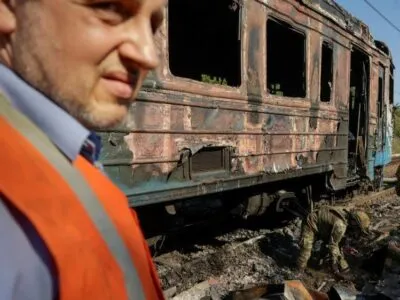 A man wearing a blue shirt and orange high vis jacket stands in front of a burnt train carriage