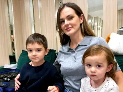 Уехать нельзя остаться. Жители Киева выбирают между добровольной эвакуацией и еще одной зимовкой в городе под обстрелами 2 Женщина с длинными волосами сидит на зеленом диване с двумя маленькими детьми, мальчиком и девочкой
