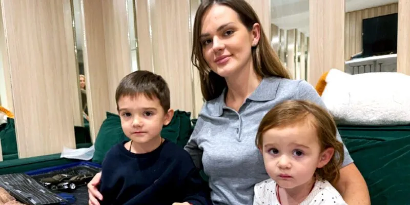 Женщина с длинными волосами сидит на зеленом диване с двумя маленькими детьми, мальчиком и девочкой